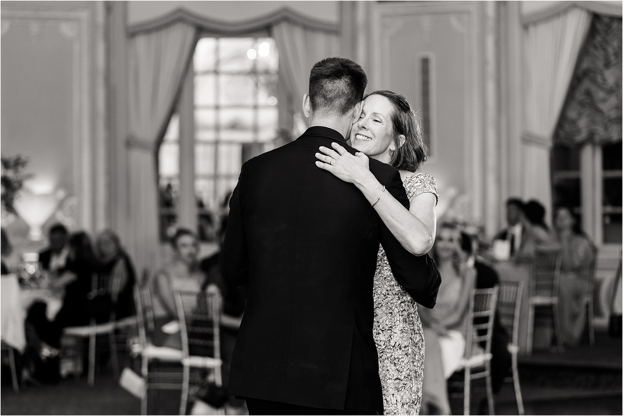 The groom's mother holding him and resting her chin on his shoulder with a smile while they have their mother son dance.