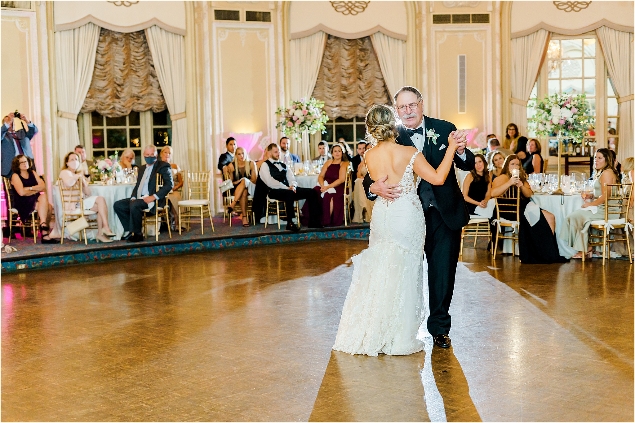 The bride dancing with her father as he is smiling during their father daughter dance.