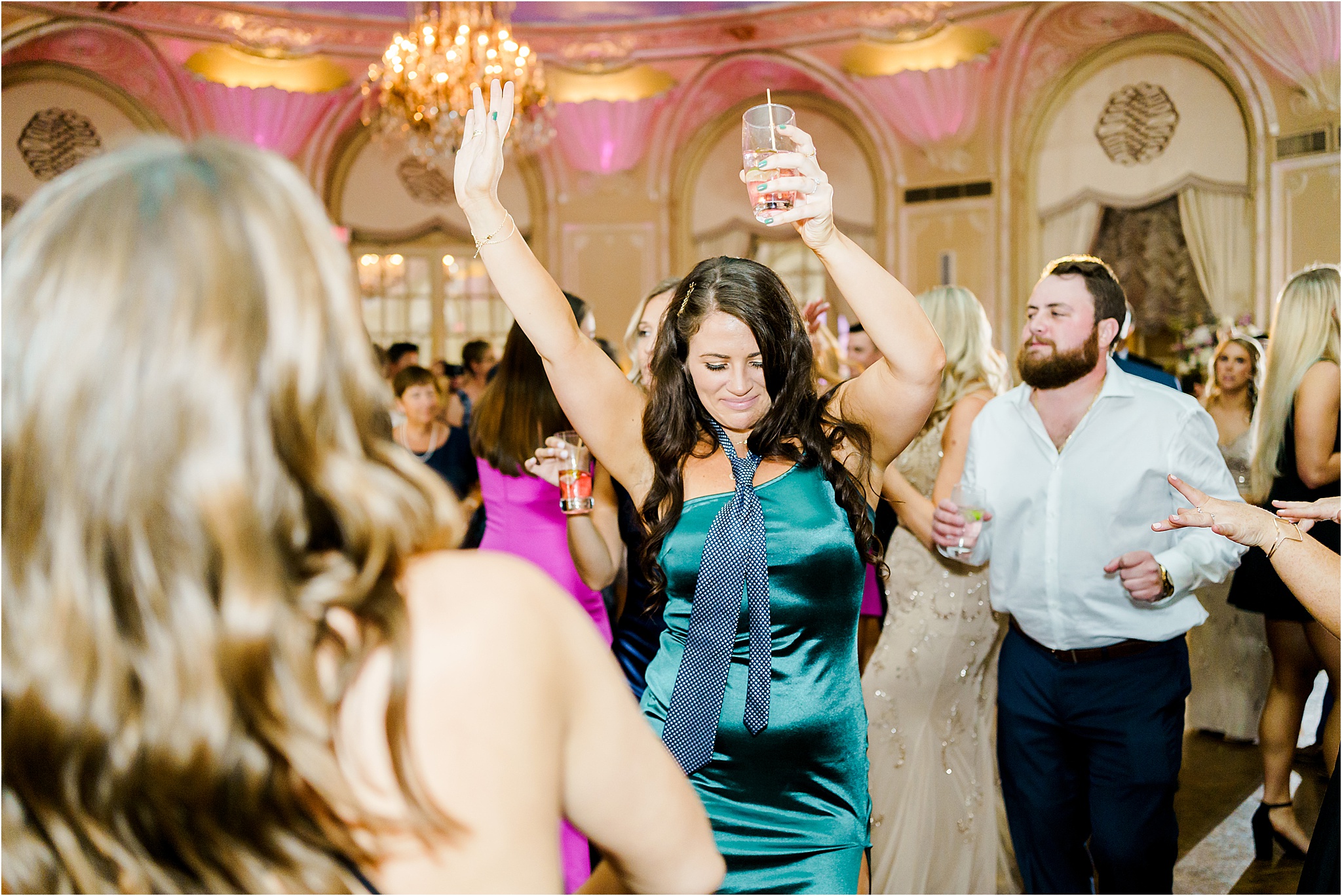 A female guest dances with her hands in the air and wearing a tie with her dress.